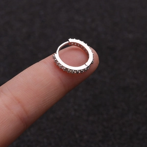 Macro shot of silver zircon small hoop earring held by fingers showing actual scale and shine