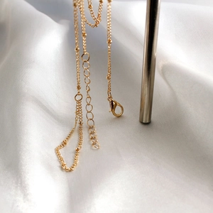 Détail du collier chaîne à billes dorées avec fermoir mousqueton sur soie blanche élégante