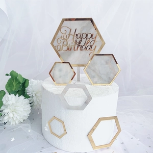 Macro view of golden Happy Birthday acrylic hexagon toppers on marble cake stand
