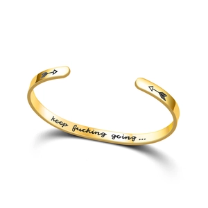 Macro detail of 'keep fucking going' engraving on a gold stainless steel cuff bracelet.