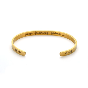 Detail of gold titanium steel cuff bracelet with 'keep fucking going' engraving.