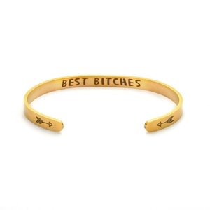 Close-up detail of a gold-tone stainless steel cuff bracelet with 'BEST BITCHES' engraving