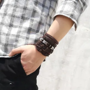 Detail of layered brown leather bracelets with woven textures and metal tube charms for men
