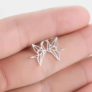 Vista macro di orecchini a gru in origami d'argento tenuti tra le dita per scala