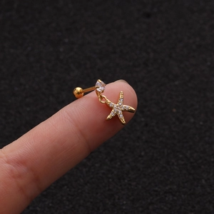 Detailed macro shot of golden starfish stud earring with zircon inlay on fingertip