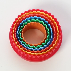 Close-up of 6 colorful round scalloped cookie cutters nested by size on a white background