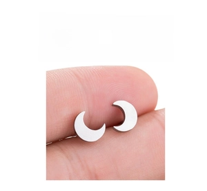 Macro detail of crescent moon stainless steel studs held to show scale and metallic finish