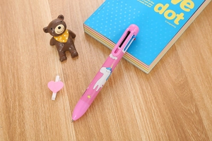 Detailed view of pink multi-color ballpoint pen with cute unicorn prints on wooden desk