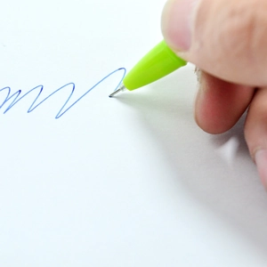 Close-up of green clover pen writing smooth blue ink lines on white paper surface