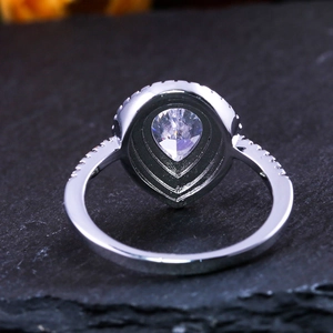 Macro shot of pear-cut zircon ring with halo pavé setting on black stone background