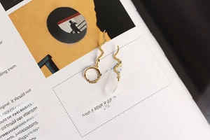 Artistic close-up of gold snake earrings resting on open book pages with text detail