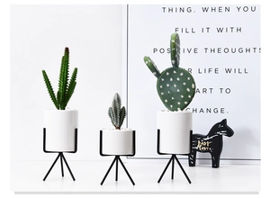 Three assorted artificial cactus plants in white ceramic pots with black metal stands