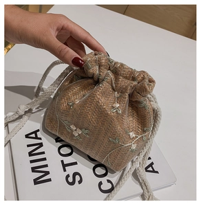 Detail of woven straw bucket bag featuring delicate floral embroidery on sheer mesh layer