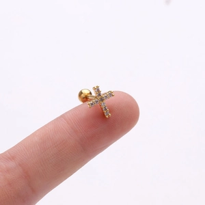 Dettaglio di un orecchino a croce dorata con zirconi tenuto sulla punta del dito