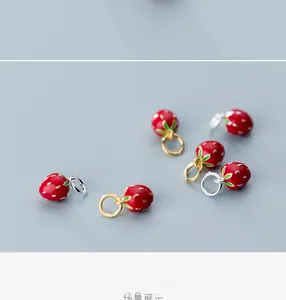 Macro view of red enamel strawberry charms with white dots and gold or silver rings