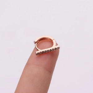 Rose gold micro-pave zircon cartilage hoop earring held on a fingertip for size