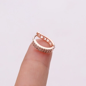 Macro view of rose gold huggie hoop earring with double row cubic zirconia on finger