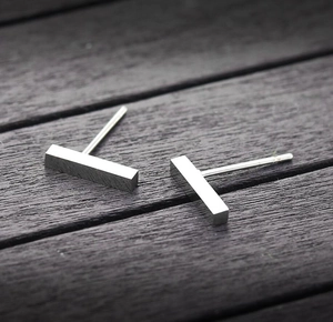 Macro view of minimalist silver vertical bar stud earrings on dark wood background