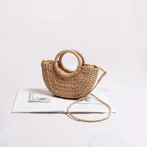 Detail of a semi-circular straw woven bag with round handles and a slim shoulder strap