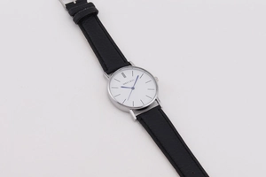 Close-up of minimalist white dial watch with blue hands and silver case on black strap