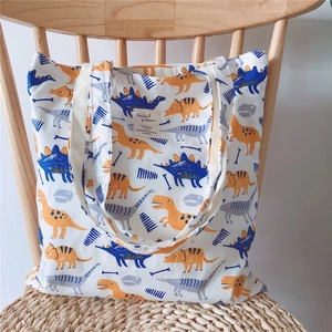 Close-up of white canvas tote bag featuring blue and orange cartoon dinosaur patterns