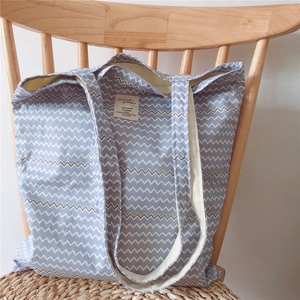 Blue and white wave pattern canvas tote bag hanging on a stylish wooden chair