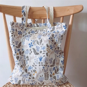 Minimalist canvas tote bag with floral and deer patterns on a wooden chair background