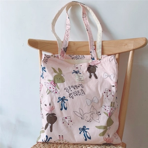 Pink canvas tote bag with rabbit patterns hanging on a wooden chair back
