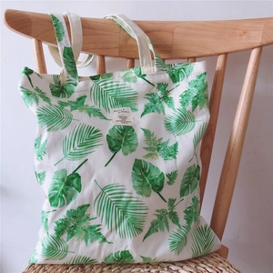 Canvas tote bag with tropical leaf pattern and dual handles on a wooden chair