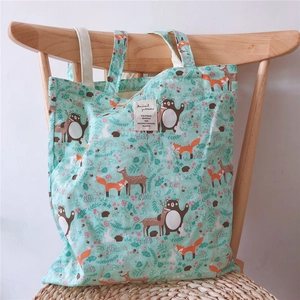 Detail of mint green cotton tote bag with forest animal prints on a wooden chair
