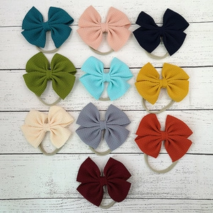 Flat lay of 10 colorful waffle texture bow headbands for babies on white wood background