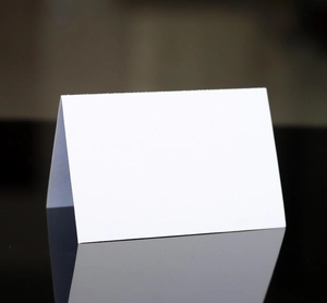 Close-up of a white folded wedding place card reflected on a black glossy surface