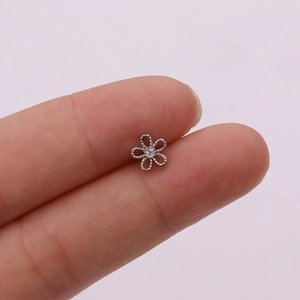 Macro shot of silver cutout flower stud earring with a small center zircon gem on a finger