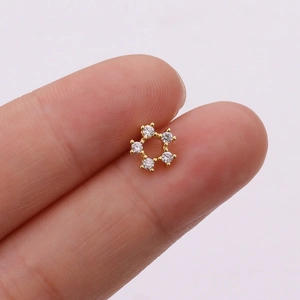 Macro shot of tiny gold star stud earring with five round zircons held on a finger