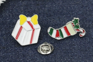 Macro shot of Christmas enamel pins featuring a gift box and stocking on blue fabric