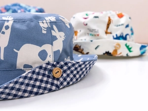 Dettaglio del cappello da pescatore per bambini in tela con stampe di animali e bottone