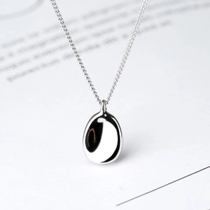 Macro shot of minimalist 925 silver necklace with polished oval pendant on book