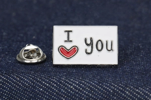 Detail of a white enamel I Love You pin with a red heart on denim fabric