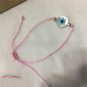 Close-up of pink woven rope bracelet with shell evil eye bead and adjustable slider