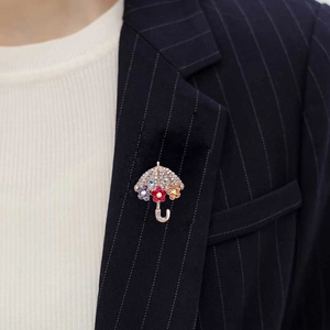 Dettaglio spilla a ombrello con cristalli e motivi floreali su un blazer blu scuro