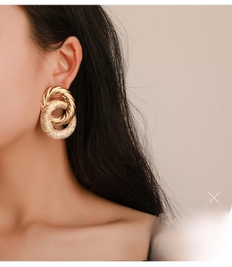 Detail of twisted gold metal C-shape hoop earrings on model with chain texture