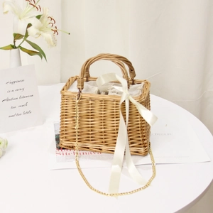 Detail of square straw handbag with white ribbon, gold chain, and natural woven texture