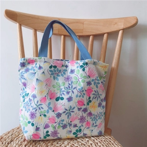 Detail einer floralen Baumwolltasche mit hellblauen Henkeln auf einem Holzstuhl