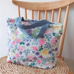 Detailaufnahme der Blumen-Stofftasche mit blauen Tragegriffen auf Korbstuhl
