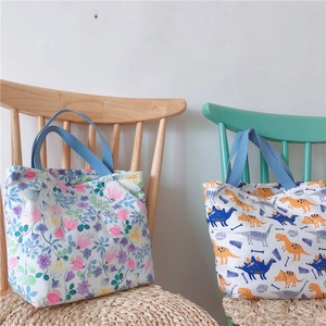 Details von Canvas-Lunchbags mit Blumen- und Dinoprint sowie blauen Tragegriffen