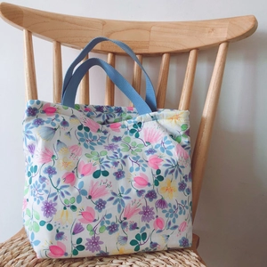 Blumige Baumwolltasche mit hellblauen Henkeln auf einem Holzstuhl in hellem Raum