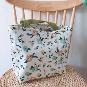 Florale Canvas-Tragetasche mit grünen Griffen auf einer Strohmatte im Garten-Stil