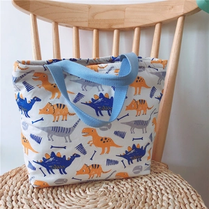 Detail eines Cartoon-Dinosaurier-Prints auf cremefarbener Canvas-Tasche mit blauem Griff