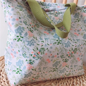 Detail der floralen Baumwolltasche mit grünen Webgriffen auf einer Strohmatte