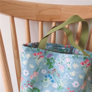 Blumige Lunchtasche an einem hellen Holzstuhl vor einer sauberen weißen Wand